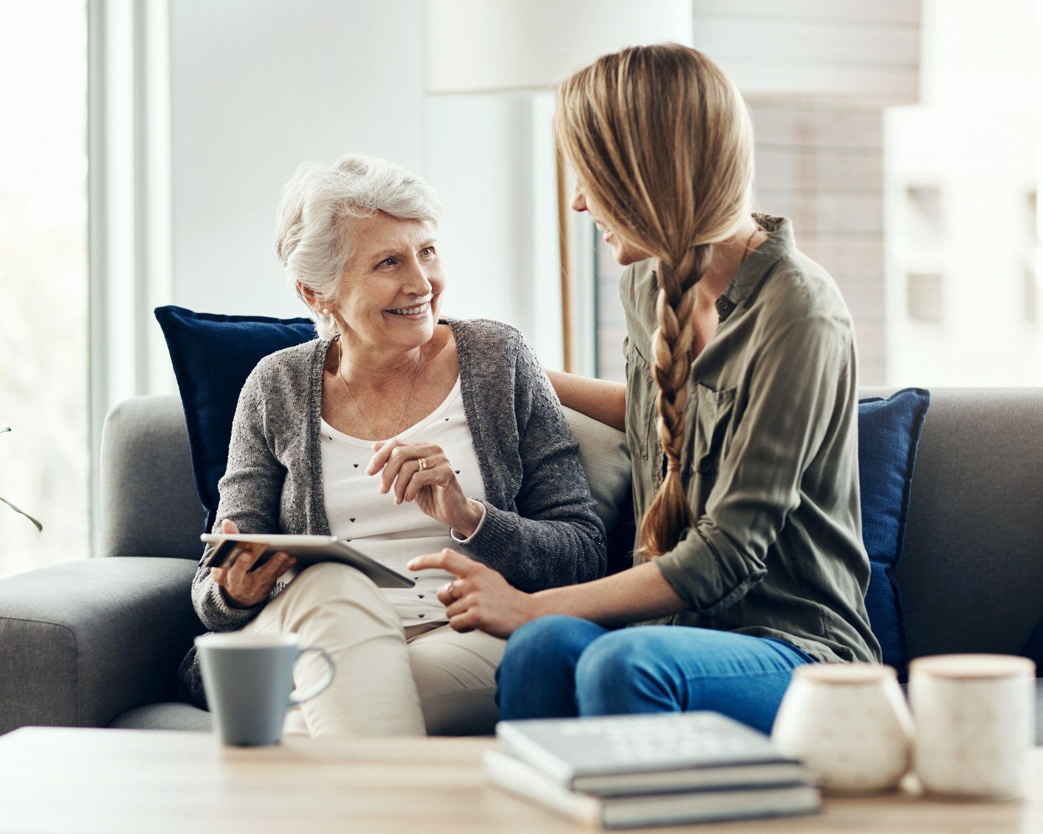 Tablet, living room and woman with senior mother in home for help with online blog, internet or connectivity. Bonding, sofa and elderly female person learning digital technology with daughter. - Trusted Life Circle | TLC App