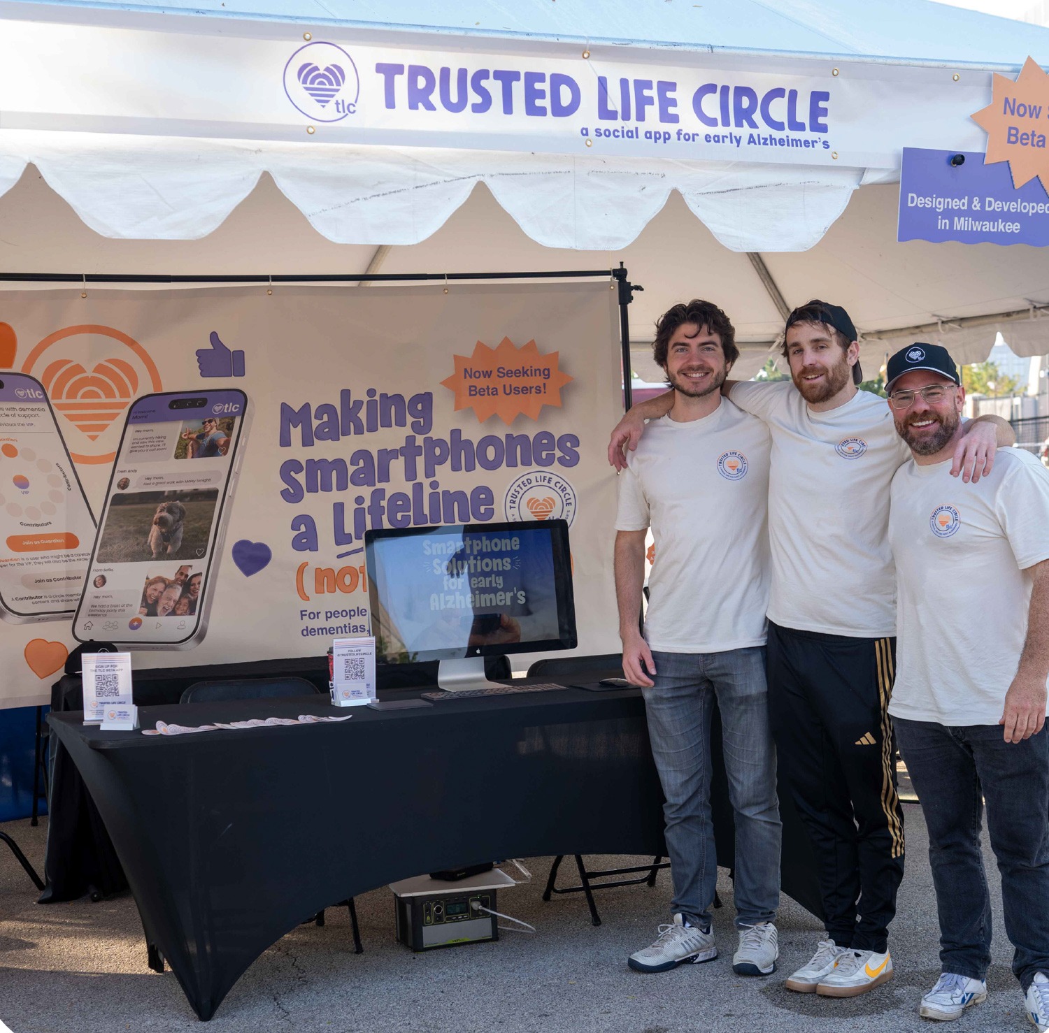 Three men in white shirts stand together at a booth for Trusted Life Circle, a social app for early Alzheimer's.